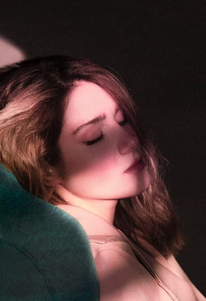 Portrait rapproché d'une femme dormant dans un train, baignée d'une lumière douce et rosée, contrastant avec un fond sombre.